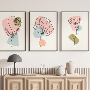May include: Three framed prints with abstract line drawings of flowers in black on a white background. Each print features a different flower with pink, blue, and green abstract shapes.