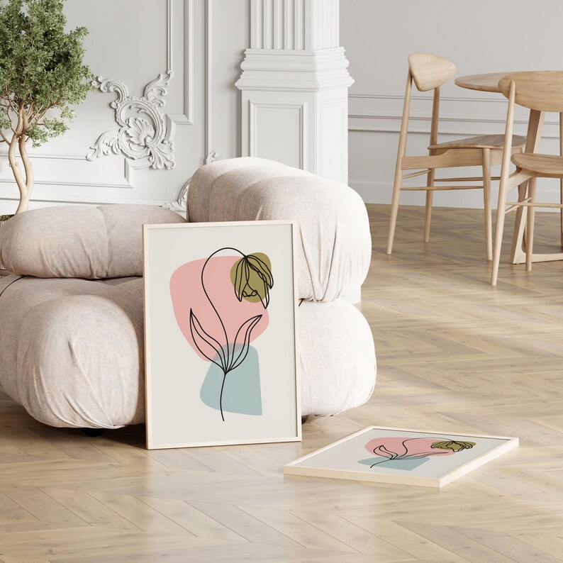 May include: A framed print of a minimalist line drawing of a flower with green and brown accents on a light background with abstract shapes in pink and blue.