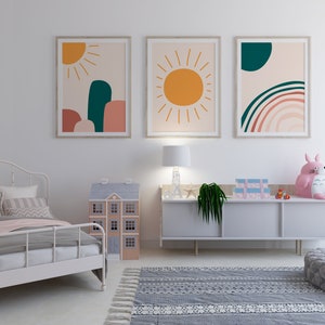 May include: A child's bedroom with a white metal bed, a dollhouse, and a gray rug. Three framed abstract art prints hang above a white dresser. A pink stuffed animal sits on the dresser. The art features sun and rainbow designs.