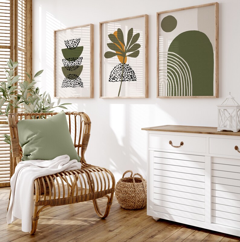 May include: A white cabinet with two drawers and two doors, a wicker chair with a green cushion, a woven basket, and three framed prints with abstract green and black designs.