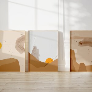 May include: Three abstract art prints in gold frames with a beige background and brown and yellow geometric shapes. The prints have a minimalist style.