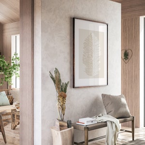 May include: A wooden bench with a light gray throw blanket and a pillow sits in a room with a light gray wall. A framed print of a beige leaf hangs on the wall above the bench. A small wooden side table with a vase of dried flowers sits next to the bench.
