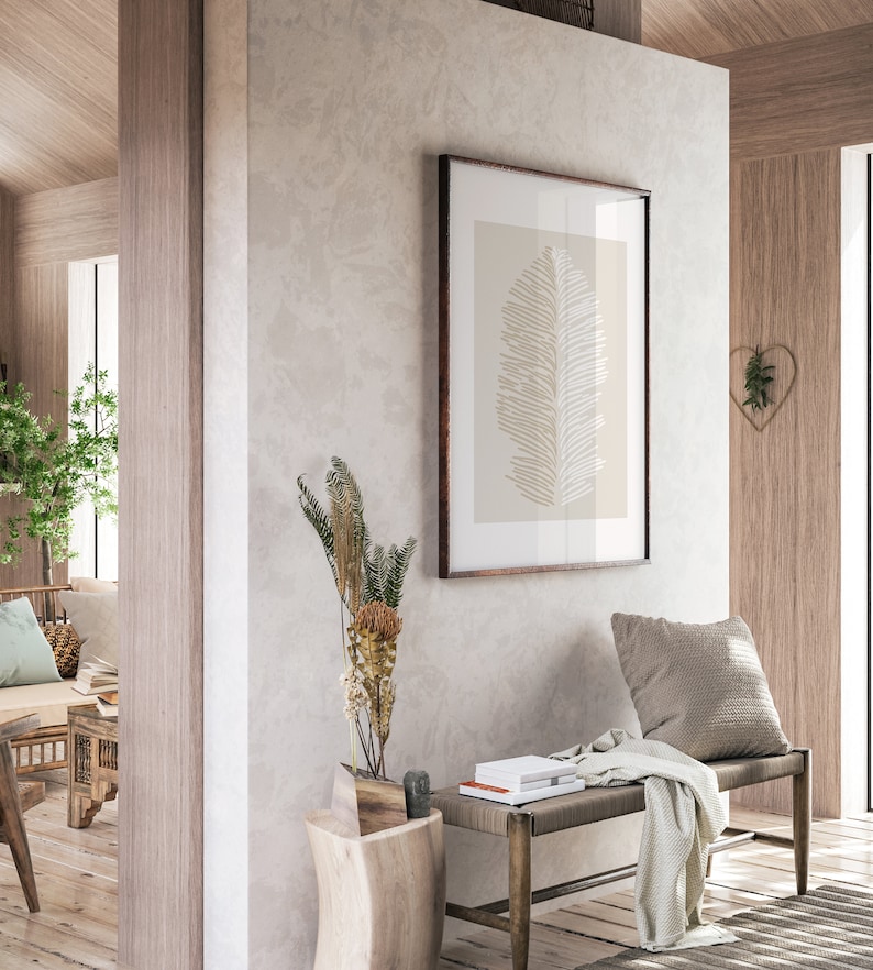 May include: A wooden bench with a light gray throw blanket and a pillow sits in a room with a light gray wall. A framed print of a beige leaf hangs on the wall above the bench. A small wooden side table with a vase of dried flowers sits next to the bench.