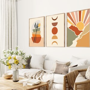 May include: Three abstract art prints in a minimalist style. The first print features a stack of bowls with a plant and chopsticks. The second print features a series of circles in shades of orange and brown. The third print features a stylised sunset with a mountain range in shades of green, orange, and brown.
