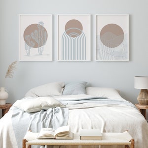 May include: Three framed abstract prints with a minimalist design. The prints feature a brown sun with blue and white geometric shapes. The prints are hung on a light blue wall above a white bed with a white blanket and pillows.