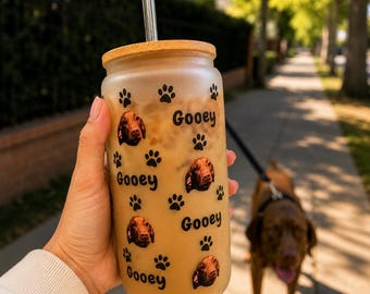 May include: A frosted glass tumbler with a bamboo lid and a clear glass straw. The exterior features a repeating pattern of black paw prints, small photographic portraits of a brown dog, and the word Gooey printed in a black sans-serif font.