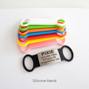 May include: A black silicone dog tag with a silver metal tag that reads "PIXIE 123-456-7890 9 Puppy St Doggieland, US". The tag is attached to a stack of colorful silicone bands.