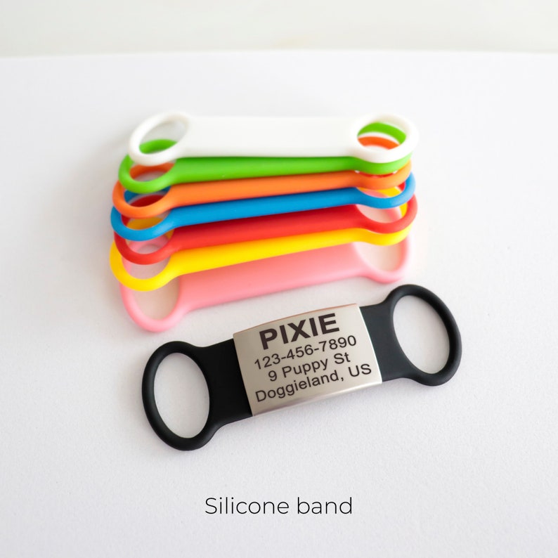 May include: A black silicone dog tag with a silver metal tag that reads "PIXIE 123-456-7890 9 Puppy St Doggieland, US". The tag is attached to a stack of colorful silicone bands.