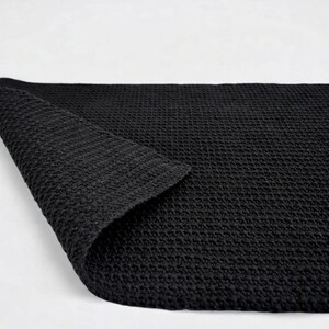 Black reversible cotton bath mat with textured surface on bathroom floor, custom size available.