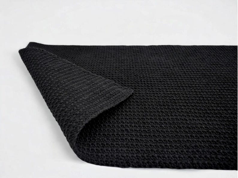 Black reversible cotton bath mat with textured surface on bathroom floor, custom size available.