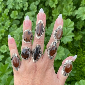 May include: A hand wearing multiple rings with oval-shaped brown and black gemstone settings. The rings are silver and have a simple design.