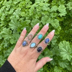 以下が含まれることがあります： 手は、楕円形の宝石がついた銀の指輪を7つ着けています。宝石は、青、ターコイズ、茶色など、さまざまな色をしています。