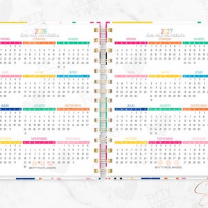 May include: A spiral-bound planner open to show 2026 and 2027 calendars with colorful monthly headers. The pages feature grid layouts for each month, the text FIFTY TWO PLANNERS, and the social media handle @FIFTYTWOPLANNERS printed at the bottom.