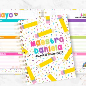 May include: A spiral-bound planner with a colourful cover featuring yellow pencils and the text "Maestra Daniela." The planner includes weekly layouts with the month of "Mayo" and the year "2026" visible. The design incorporates rainbow accents and a playful, educational theme.