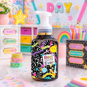 May include: A black soap dispenser with a white pump top, decorated with a colorful design. The design includes a smiley face, rainbow, and the text "Best Teacher Ever." The dispenser has a gold-colored band near the top.