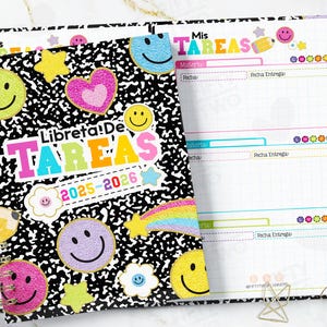 Puede incluir: Una agenda de espiral con una cubierta moteada en blanco y negro, adornada con pegatinas de caras sonrientes de colores, estrellas y un corazón. La portada dice "Libreta! De Tareas 2025-2026". Las páginas abiertas muestran una lista de tareas con secciones para materiales y plazos.