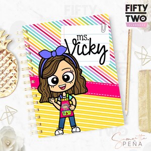 May include: Spiral-bound planner with a colorful striped cover and the text "ms. Vicky." The cover features a cartoon illustration of a smiling teacher wearing an apron. The planner has a gold spiral binding.