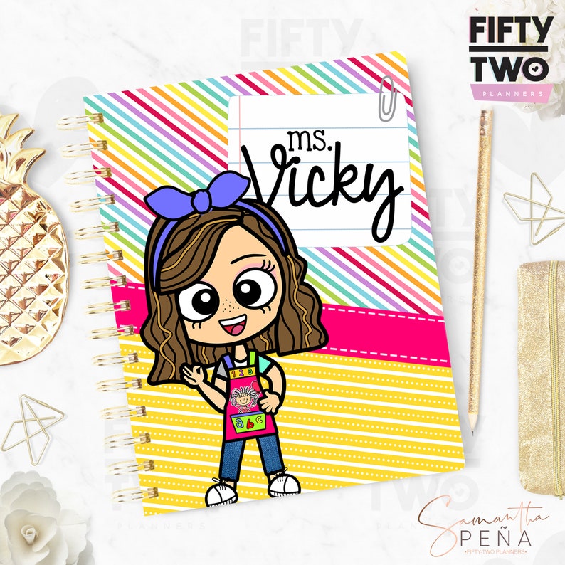 May include: Spiral-bound planner with a colorful striped cover and the text "ms. Vicky." The cover features a cartoon illustration of a smiling teacher wearing an apron. The planner has a gold spiral binding.