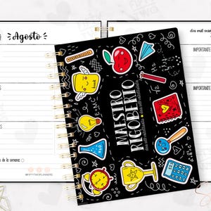 May include: A spiral-bound planner with a black cover featuring colorful school-themed stickers. The planner is open to show the month of August, with dates and space for notes. The text "MAESTRO RIGOBERTO" is visible on the cover.