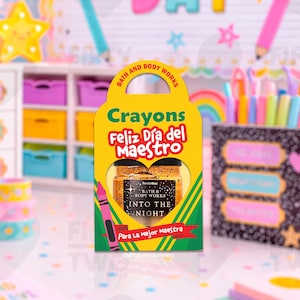 May include: A yellow crayon-shaped gift box with the text "Crayons Feliz Día del Maestro" and "Bath & Body Works Into The Night." The box contains two small jars. A pink crayon is on the left side of the box. The background includes colorful decorations.