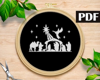 May include: A black and white cross-stitch pattern of the nativity scene with a star, angel, and three wise men. The pattern is in a wooden embroidery hoop.