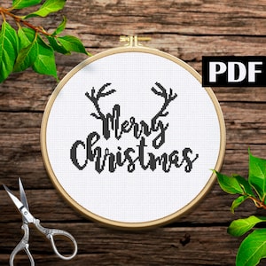 May include: A white embroidery hoop with black embroidery of the text "Merry Christmas" with reindeer antlers above the text.