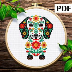 Puede incluir: Un patrón de punto de cruz de un perro salchicha con un diseño floral. El perro tiene orejas negras con flores rojas y amarillas, y una cara blanca con detalles florales verdes y amarillos. El texto "PDF" está en la esquina superior derecha.