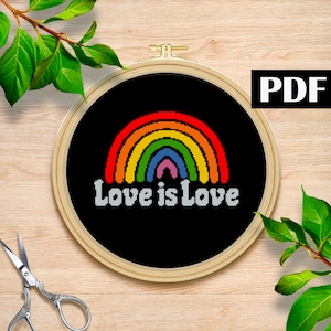 May include: A cross-stitch design featuring a rainbow arch over the words "Love is Love" in white. The design is set against a black background and framed in a wooden embroidery hoop. The word "PDF" is in a black rectangle.