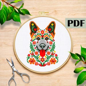 May include: A cross-stitch pattern of a dog's head, adorned with floral designs in red, orange, yellow, and green. The dog's face is gray, with its tongue sticking out. The pattern is in a wooden embroidery hoop. The word "PDF" is in the upper right corner.