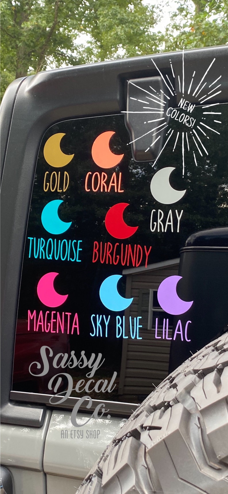 May include: A black car window with a variety of moon-shaped decals in different colors, including gold, coral, gray, turquoise, burgundy, magenta, sky blue, and lilac. The decals are arranged in rows and are labeled with their corresponding colors. The text "NEW COLORS!" is also visible on the window. The text "Sassy Decal Co. AN ETSY SHOP" is visible at the bottom of the window.