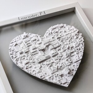 May include: A white 3D printed heart-shaped map of Lancaster, PA, framed in a white frame with a glass front. The date "September 5th, 2023" is inscribed on the bottom of the frame.