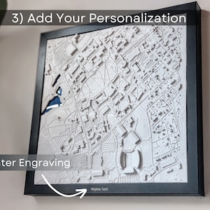 K&ouml;nnte beinhalten: Eine wei&szlig;e 3D-gedruckte Karte einer Stadt mit einem schwarzen Rahmen. Die Karte ist an einer Wand montiert. Der Text "Enter Engraving" ist in der linken unteren Ecke des Bildes sichtbar. Der Text "Virginia Tech" ist in der rechten unteren Ecke des Bildes sichtbar.