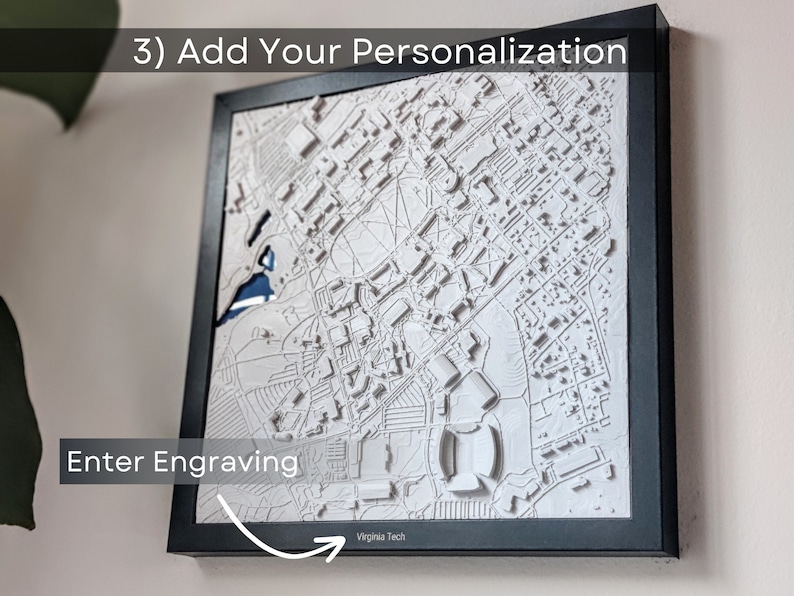 K&ouml;nnte beinhalten: Eine wei&szlig;e 3D-gedruckte Karte einer Stadt mit einem schwarzen Rahmen. Die Karte ist an einer Wand montiert. Der Text "Enter Engraving" ist in der linken unteren Ecke des Bildes sichtbar. Der Text "Virginia Tech" ist in der rechten unteren Ecke des Bildes sichtbar.