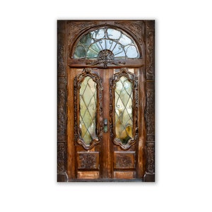 May include: A detailed, antique wooden door with intricate carvings and leaded glass panels. The door features a half-circle window above the two main doors, adding to its ornate design. The wood has a rich, warm brown tone.