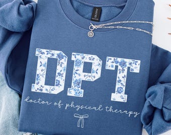 Könnte beinhalten: Ein indigoblaues Sweatshirt mit Rundhalsausschnitt und den Blockbuchstaben DPT, die mit einem weiß-blauen Blumenmuster gefüllt sind. Unter den Buchstaben steht in weißer Schreibschrift doctor of physical therapy und eine kleine weiße Schleife.