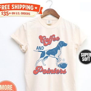 May include: Ivory-colored t-shirt with the text "Coffee and Pointers" and a blue and white dog graphic. The shirt also has the words "More Colors" and "Super Soft" printed on it.