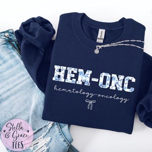 May include: Navy blue sweatshirt with a white floral design and the text "HEM-ONC hematology-oncology".