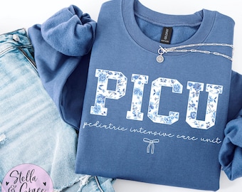 May include: A blue sweatshirt with the words "PICU Pediatric Intensive Care Unit" printed on the front. The letters are decorated with a white floral pattern.