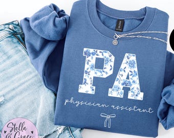 May include: A blue sweatshirt with the letters PA in white with a floral pattern. The text "physician assistant" is written below the letters.
