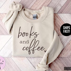 May include: Sand-colored sweatshirt with the words "books and coffee" in a dark brown script. The sweatshirt has a crew neck and long sleeves. The brand name "Stella & Grace Tees" is in a pink circle.