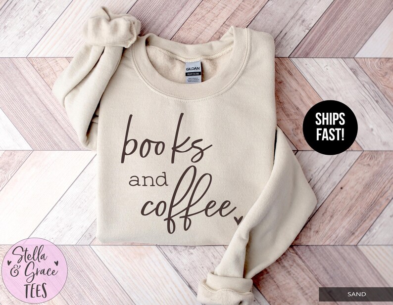 May include: Sand-colored sweatshirt with the words "books and coffee" in a dark brown script. The sweatshirt has a crew neck and long sleeves. The brand name "Stella & Grace Tees" is in a pink circle.