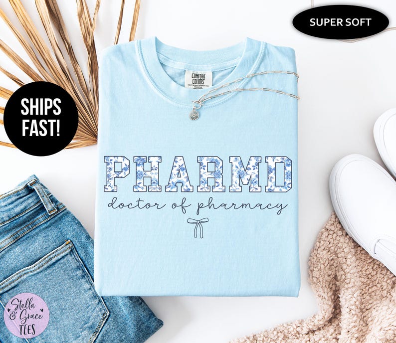 Puede incluir: Camiseta azul claro con un dise&ntilde;o de estampado floral que dice "PHARMD doctor of pharmacy" en una fuente universitaria.