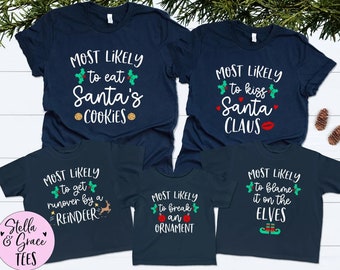 May include: Navy blue t-shirts with white text and Christmas-themed graphics. The shirts read "Most Likely to eat Santa's Cookies," "Most Likely to kiss Santa Claus," "Most Likely to get runover by a Reindeer," "Most Likely to break an Ornament," and "Most Likely to blame it on the Elves."