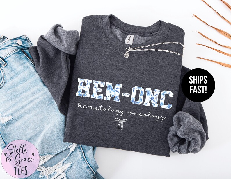 May include: Dark grey sweatshirt with the text "HEM-ONC hematology-oncology" in white with blue floral accents.