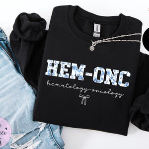 May include: Black sweatshirt with the text "HEM-ONC hematology-oncology" in white with blue floral accents.