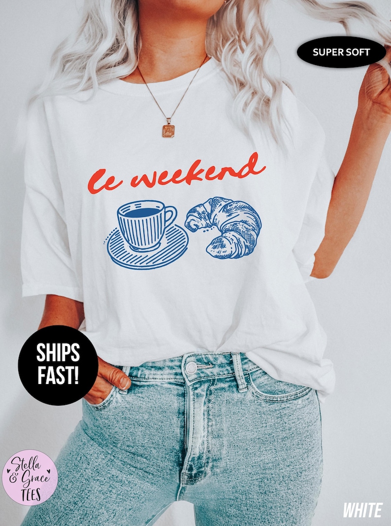 May include: White t-shirt with the phrase "le weekend" in red script, along with a blue illustration of a coffee cup and croissant. The shirt is labeled "Super Soft" and "White".