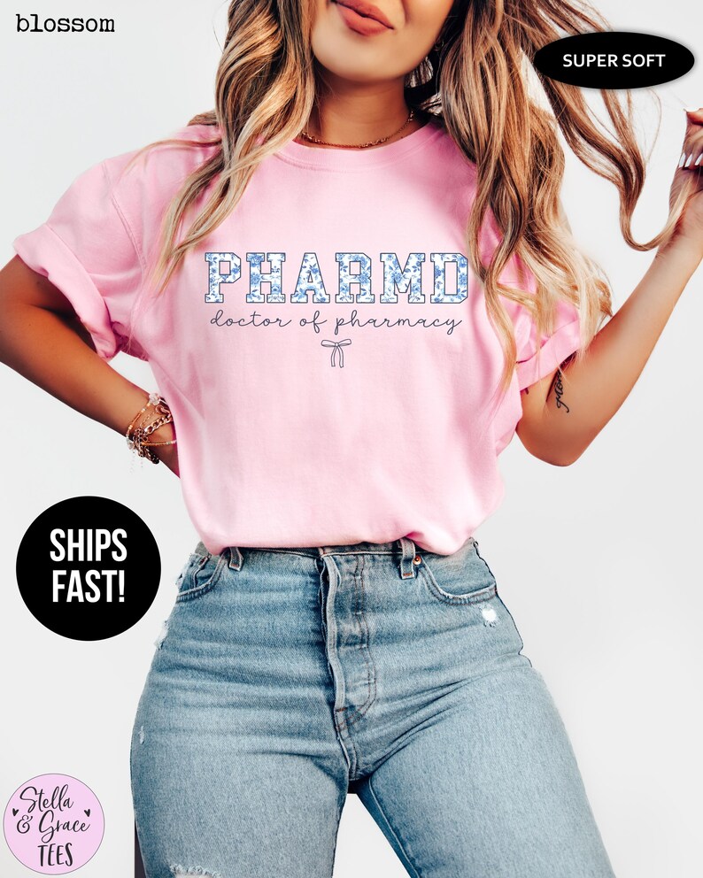 Puede incluir: Camiseta rosa con el texto "PHARMD doctor of pharmacy" en letras azules con contorno blanco. La camiseta tiene un patr&oacute;n floral en azul y blanco.