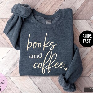 May include: Dark grey heather sweatshirt with the words "books and coffee" in a cream-colored script. The sweatshirt has a crew neck and long sleeves. The text "SHIPS FAST!" is in a black circle.