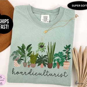 Op de afbeelding: Lichtgroen t-shirt met een botanische illustratie en het woord "hoardiculturist". Het ontwerp toont diverse potplanten in verschillende vormen en maten. Het shirt heeft een ronde hals en korte mouwen.