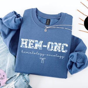 May include: A blue sweatshirt with the text "HEM-ONC hematology-oncology" in white with a floral pattern.